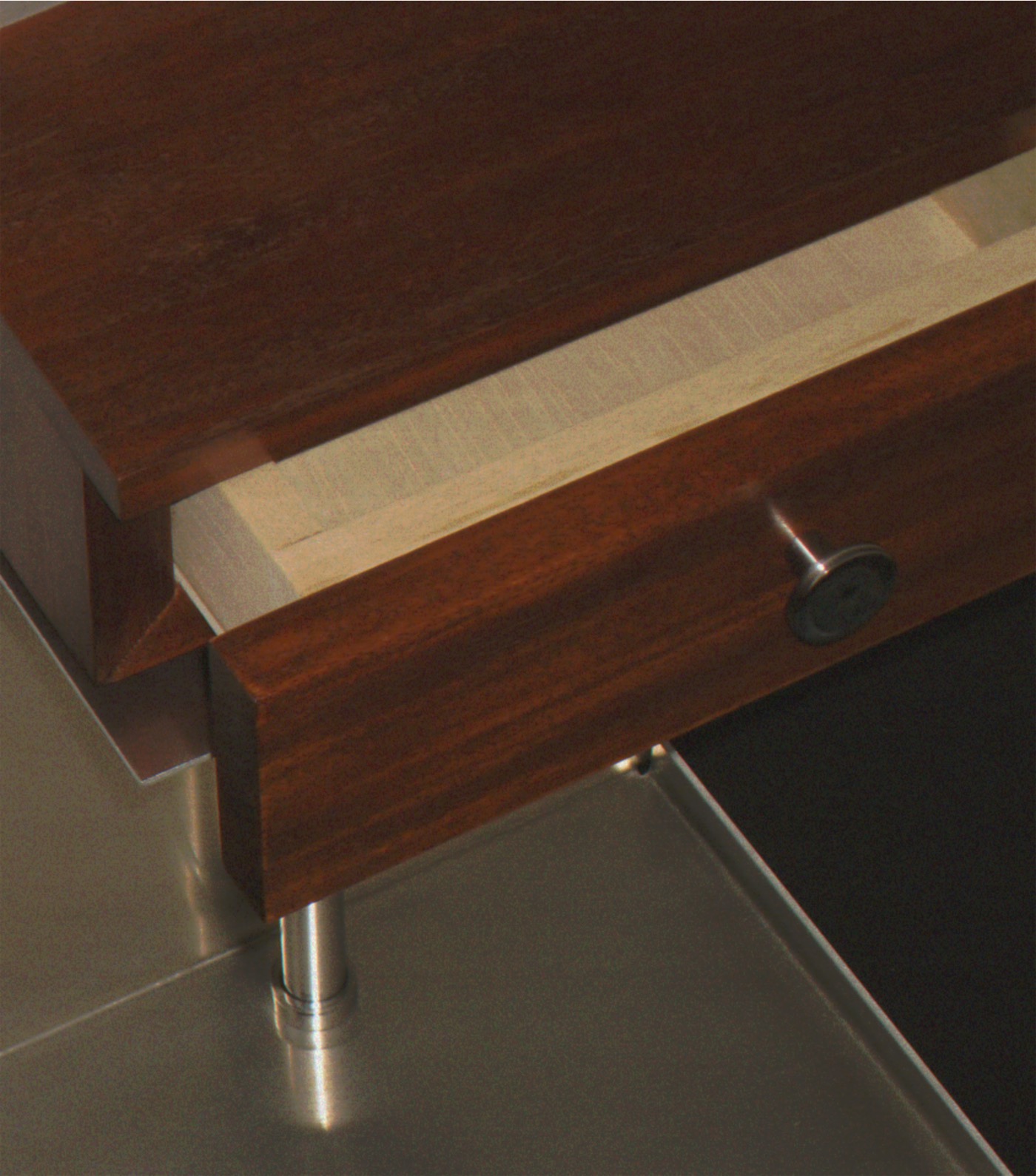 Close-up of the drawer pulled open, showing its pale wood interior, round pull, and a steel post below.
